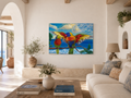A colorful luxury interior artwork canvas painting of two parrots perched on a branch over a blue ocean, displayed on a white wall in a bright, modern living room with a sofa, coffee table, and potted plants.